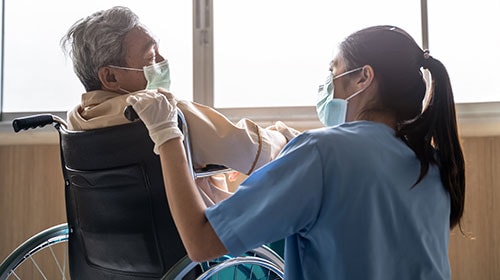 Nurse taking care of an older male patient sitting in a wheelchair in a long-term care facility