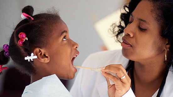 Image of a doctor examining the throat of a young child with a tongue depressor.