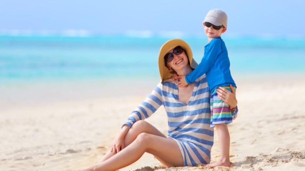Photo of a mother and her young son wearing hats and sunglasses on the beach