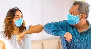 man and woman wearing facial masks and touching elbows