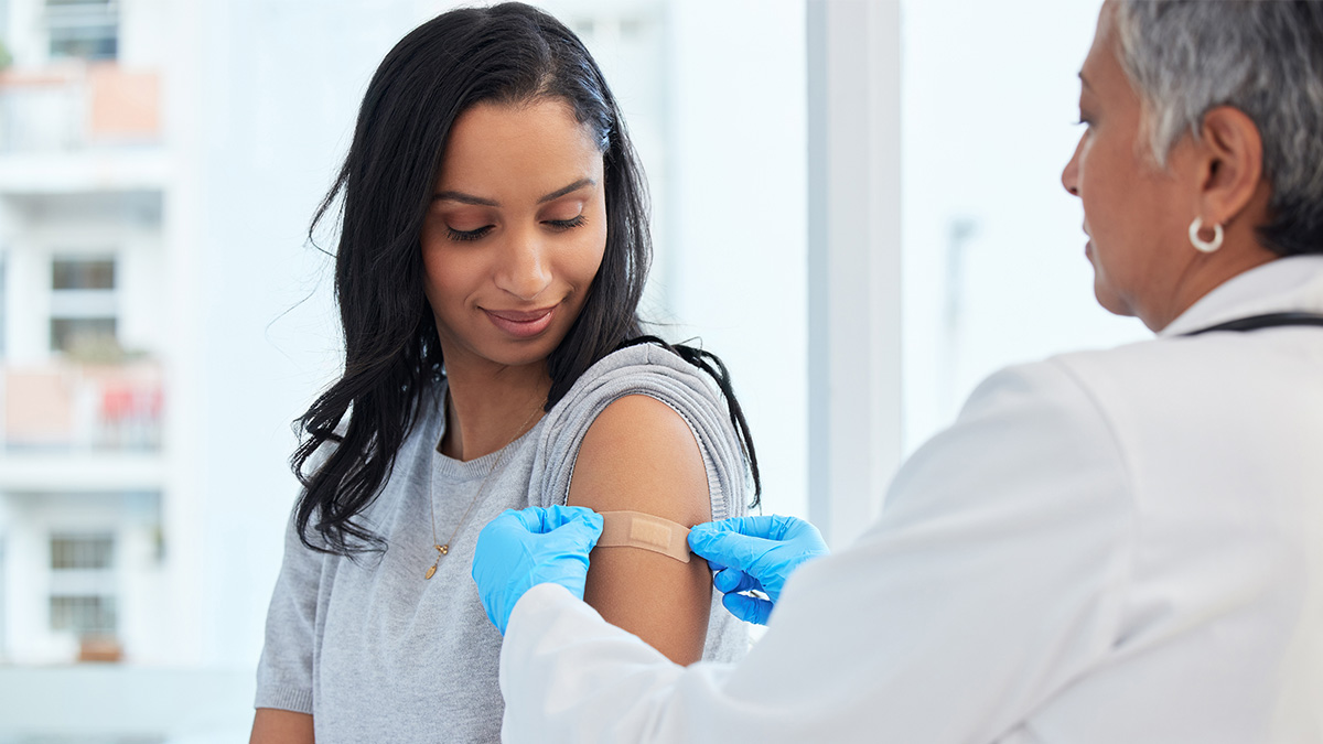 A doctor placing a bandage over the vaccination site on a patient's arm