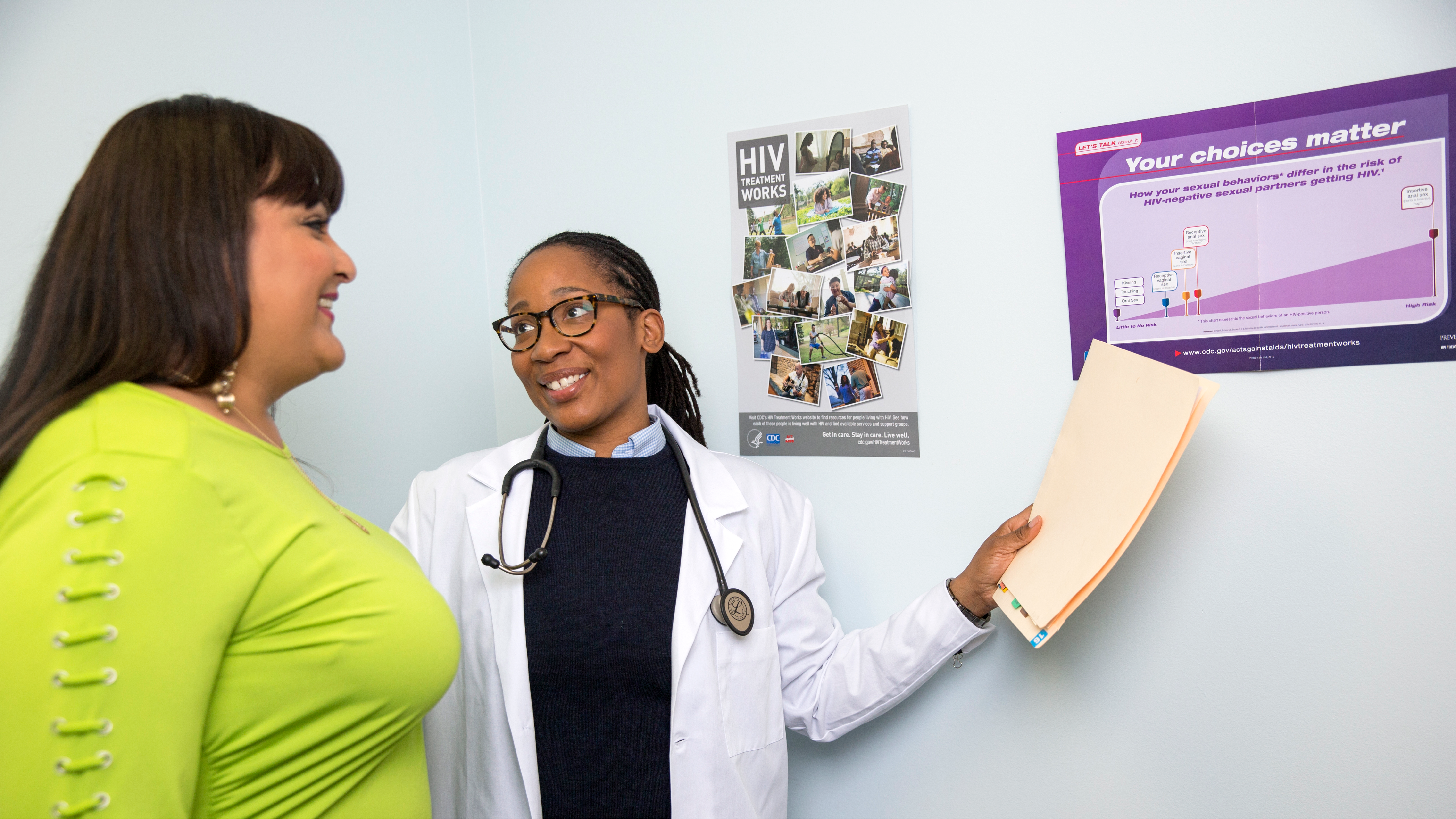 A health care provider talking to a patient while pointing to wall poster with information about HIV.