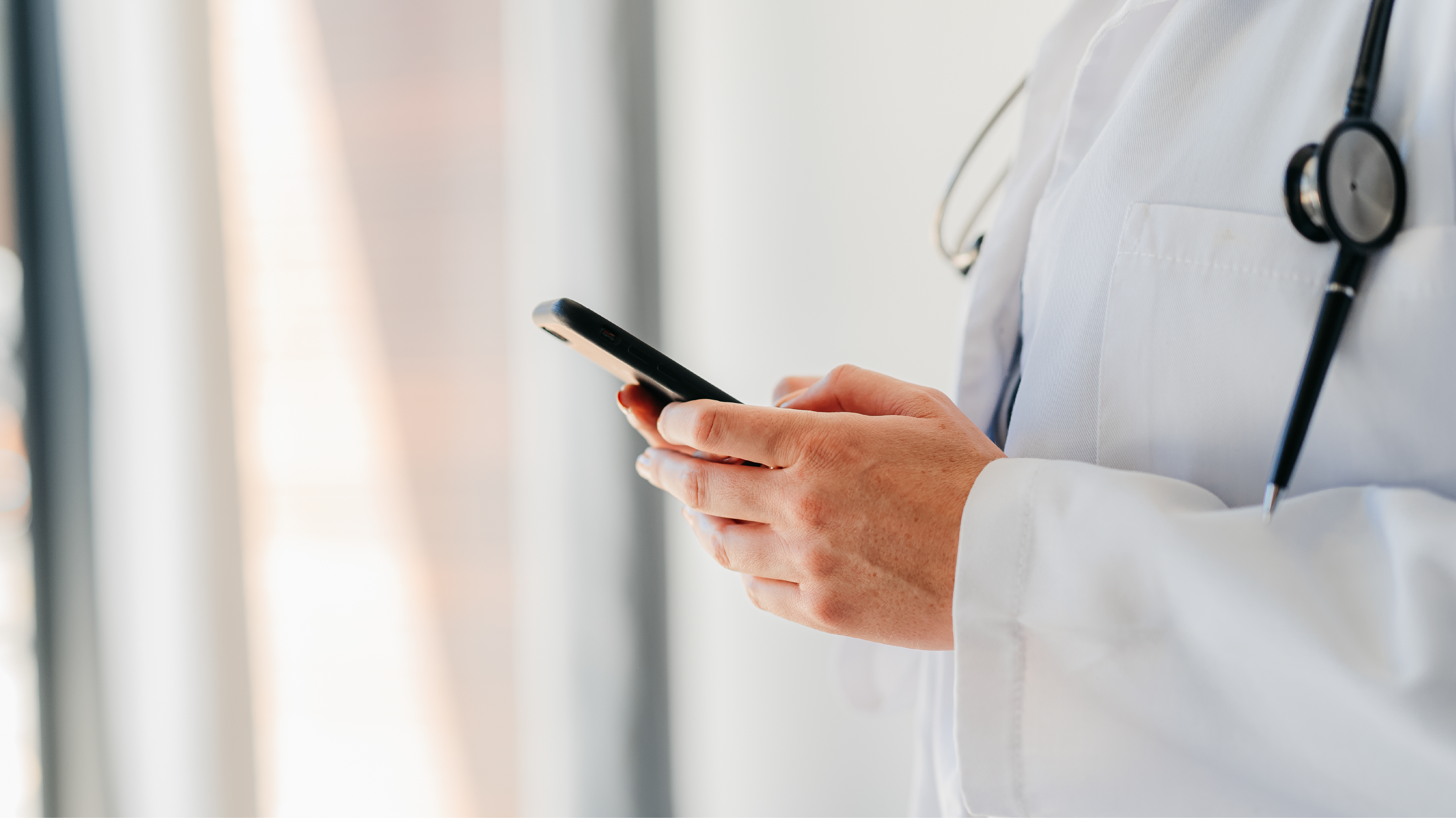A health care provider with a stethoscope typing on a smart phone.