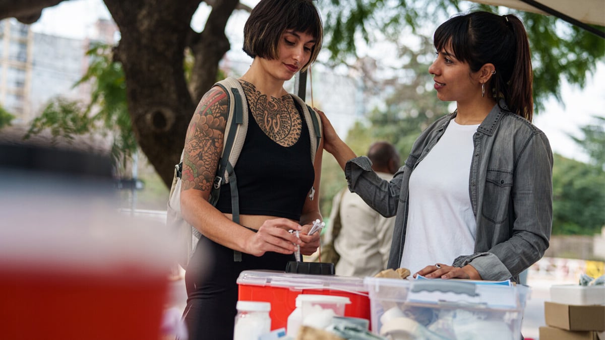 A woman with tattoos safely disposes used syringes at a syringe services program (SSP) site.