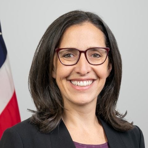 Deputy Director for Policy, Communications, and Legislative Affairs/Chief Strategy Officer Andi Lipstein Fristedt. An American flag is behind her.