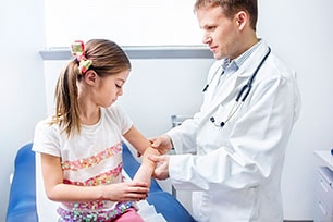 Médico examinando el codo de una niña.