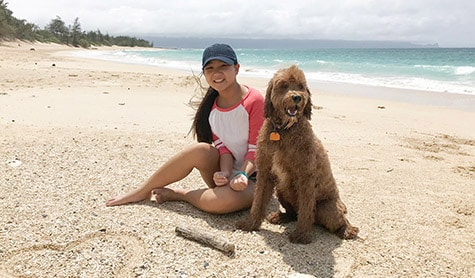 Emma sits on the beach with her dog.