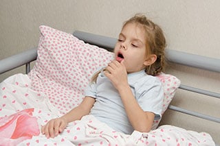Girl lying in bed coughing.