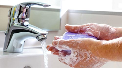 Washing hands under a faucet with soap and water.