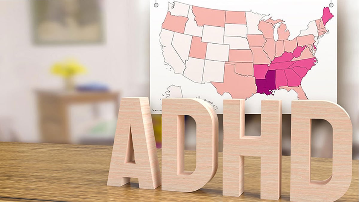 Wooden block letters spelling out "ADHD" placed in front of a U.S. map showing estimates of ADHD by state.