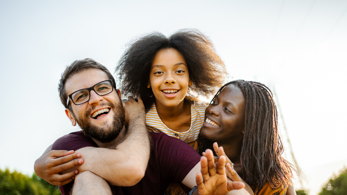 Two parents outside with their daughter on their shoulders smiling.