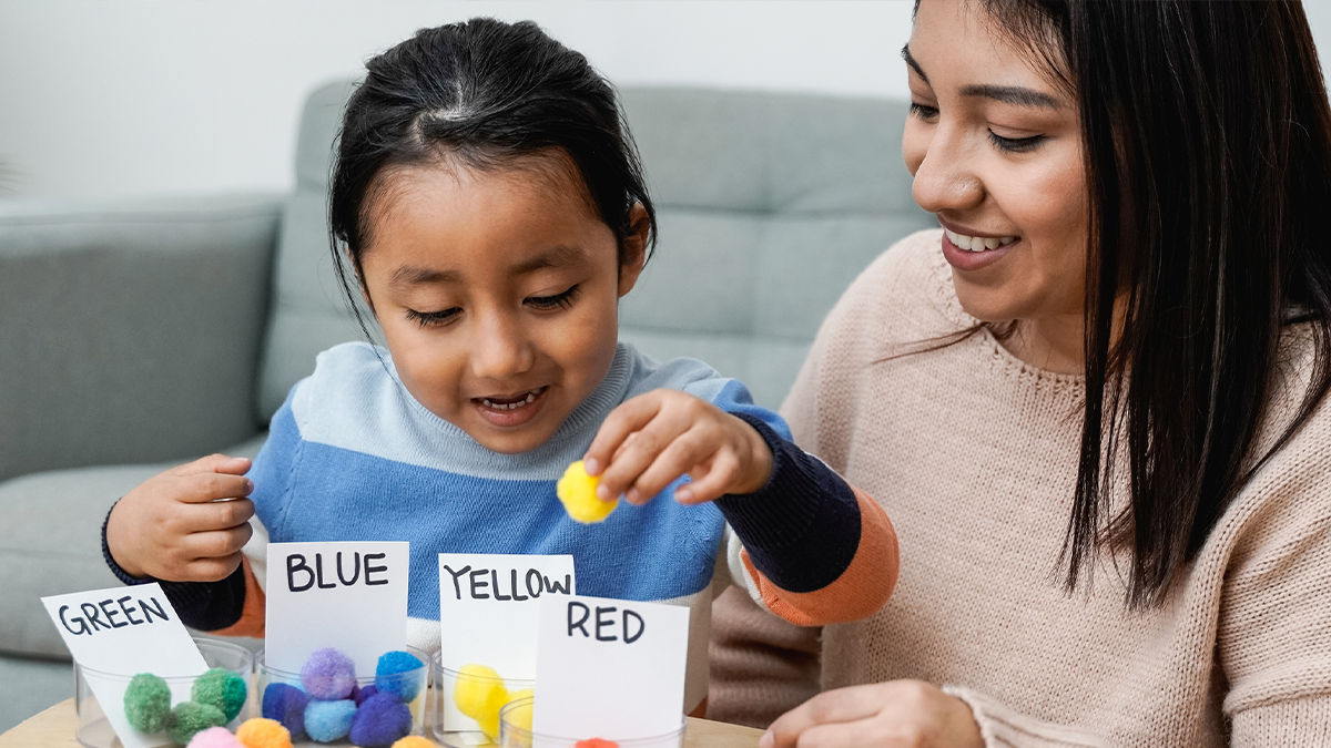 A child learning colors with a teacher on a small table