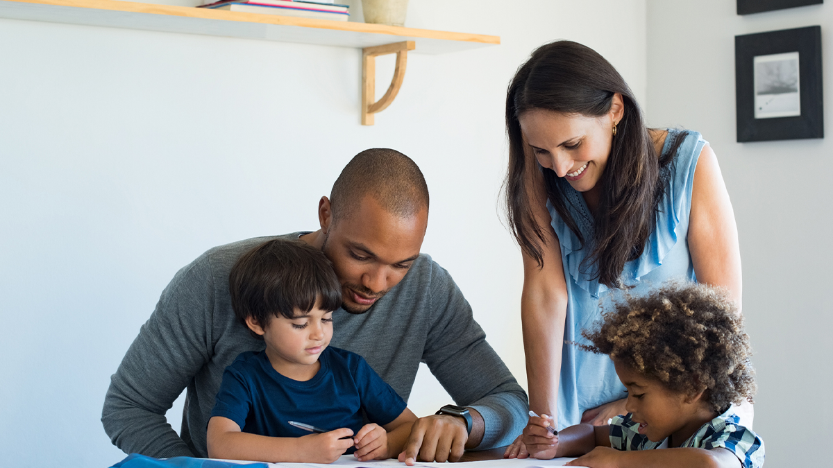 Padre y madre ayudando a sus dos hijos con las tareas escolares