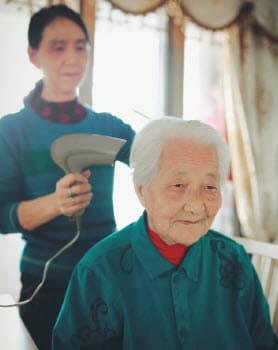 Younger woman blow drying elder woman's hair