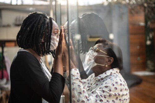 Masked mother and daughter talking through glass wall