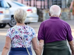 elderly couple holding hands walking down a street