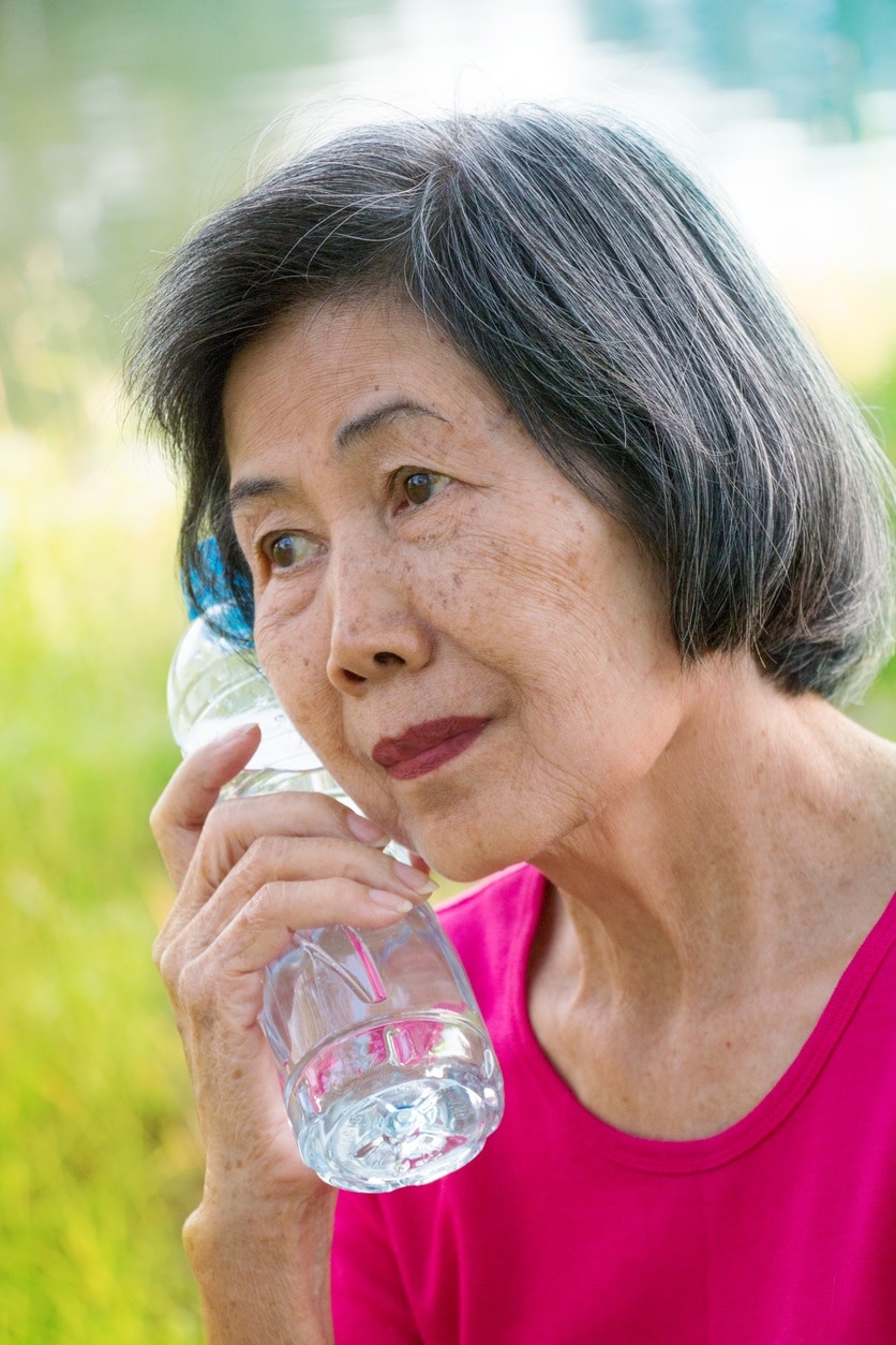 Senior Asian lady holding a water bottle to her face