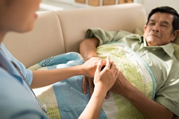 Caregiver holding the hands of an elderly man lying in bed.