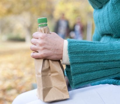 Female on park bench with bottle of alcohol in paper bag