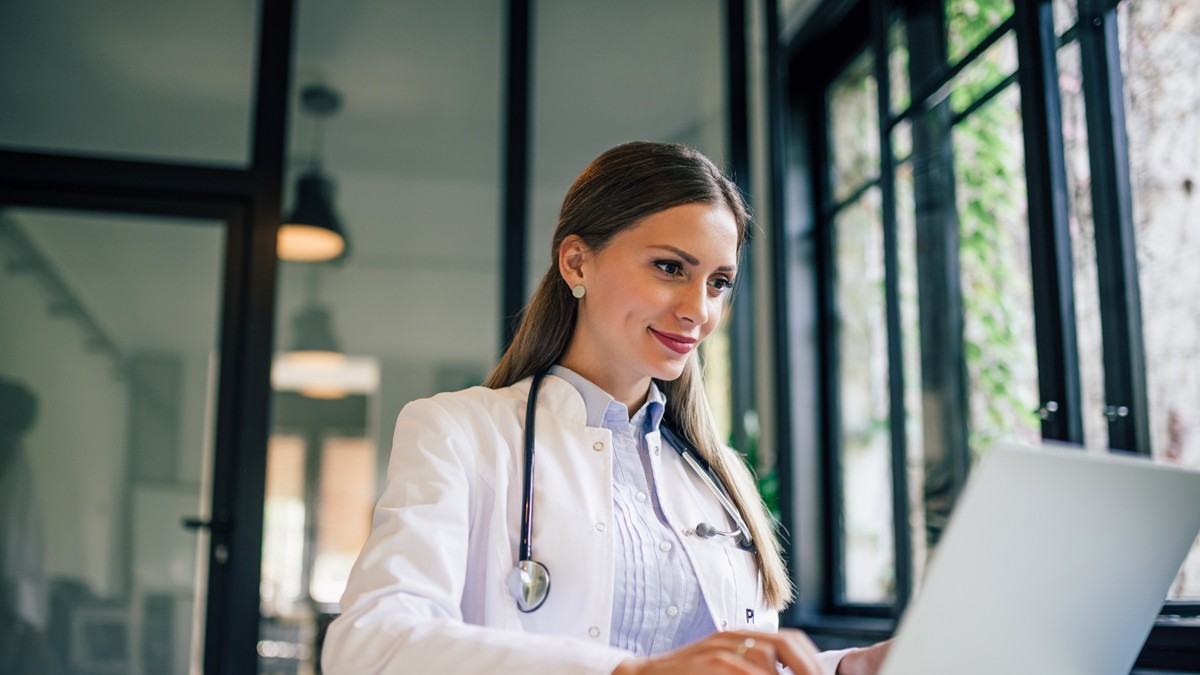 Una profesional de la salud sentada frente a su computadora y tomando un curso de educaci&oacute;n continua.