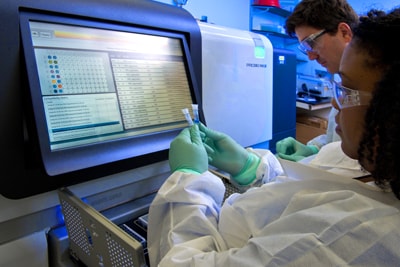 Two lab scientists preparing vials for sequencing using a large machine
