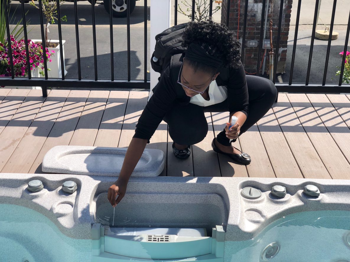 a woman kneels beside a hot tub with a swab in one hand and a sample container in the other