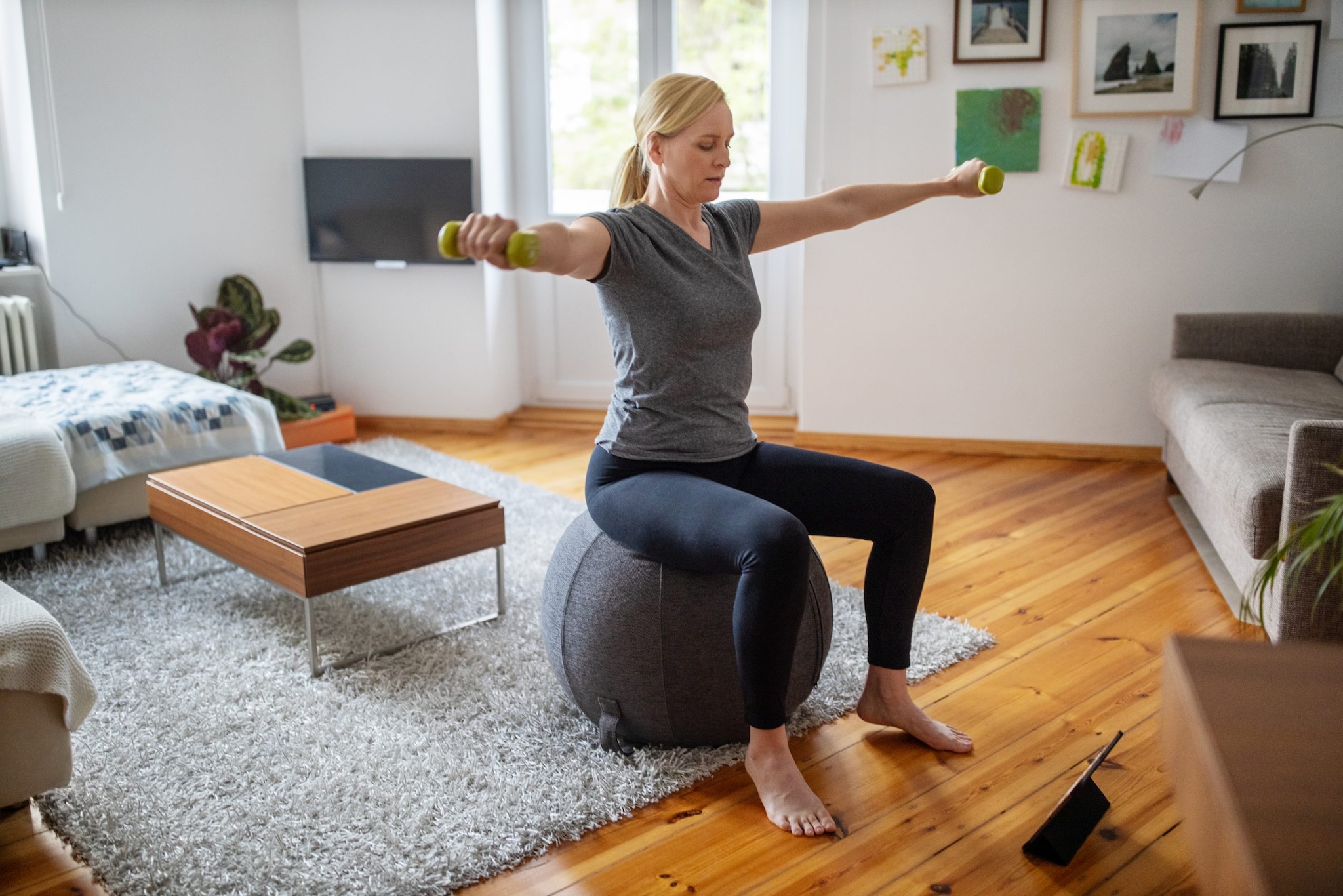 Una mujer sentada sobre una pelota de ejercicio en la sala y haciendo ejercicio con pesas.