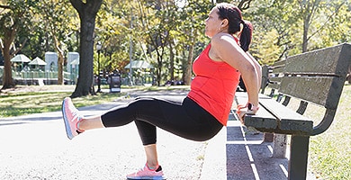 Woman with arthritis exercising by doing reverse dips on park bench