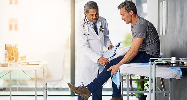 Doctor helping adult male patient with arthritic knee.