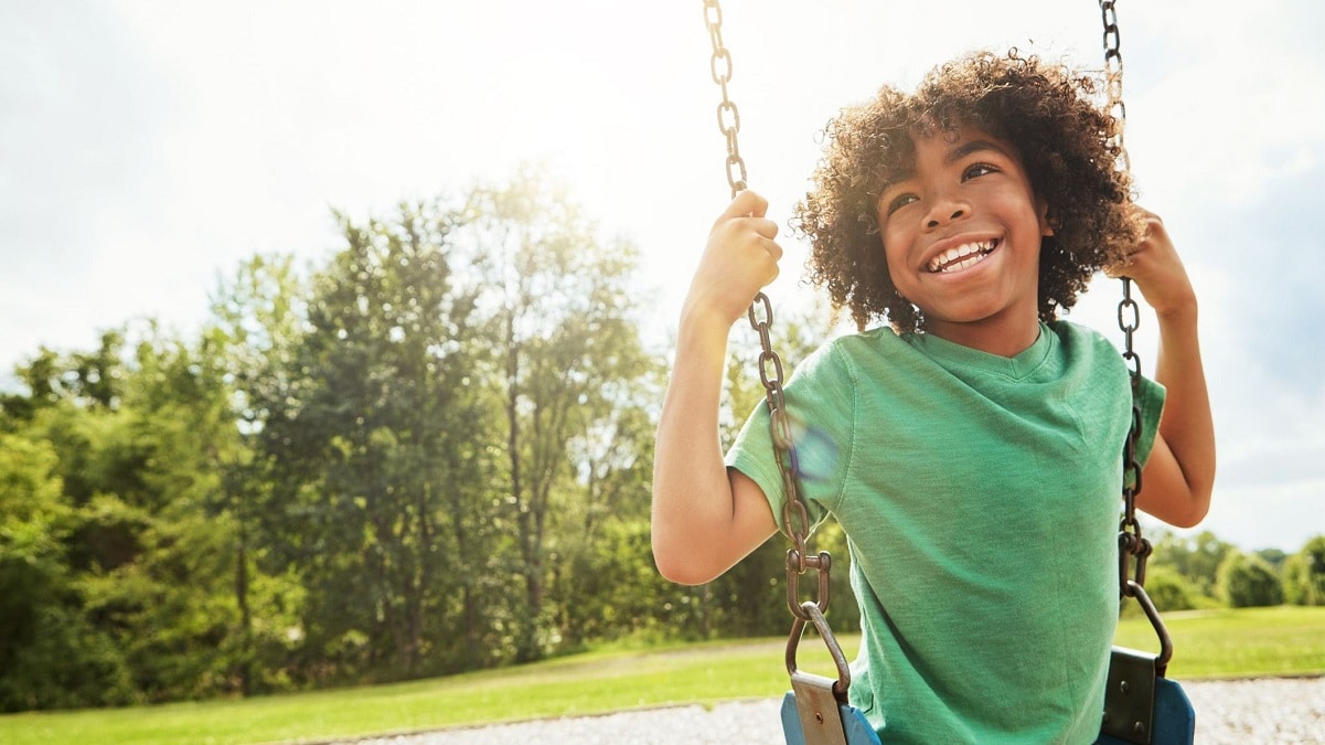 Kid sitting on a swing and smiling