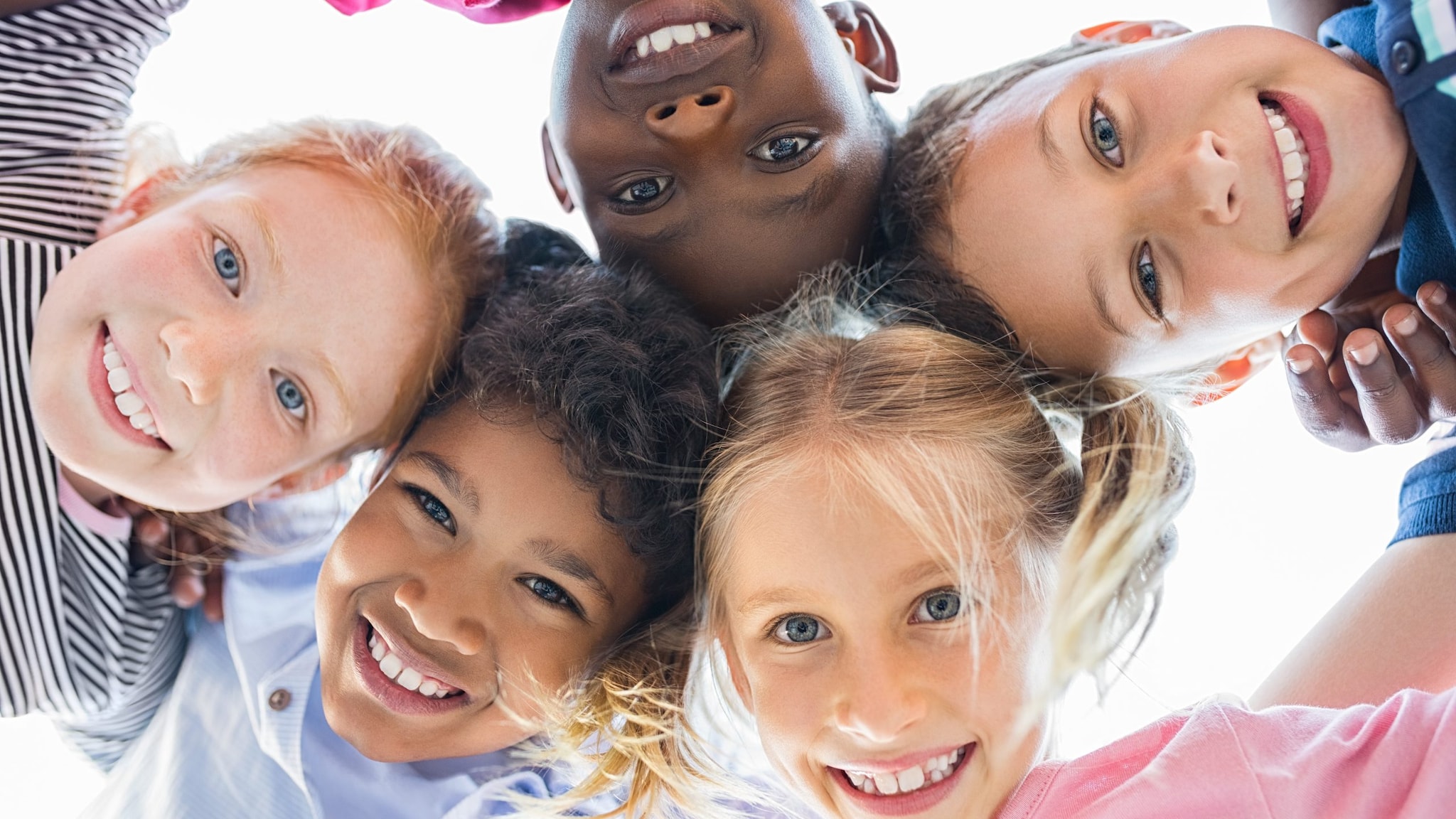 Five ethnically diverse children in a circle smiling happily down toward camera.