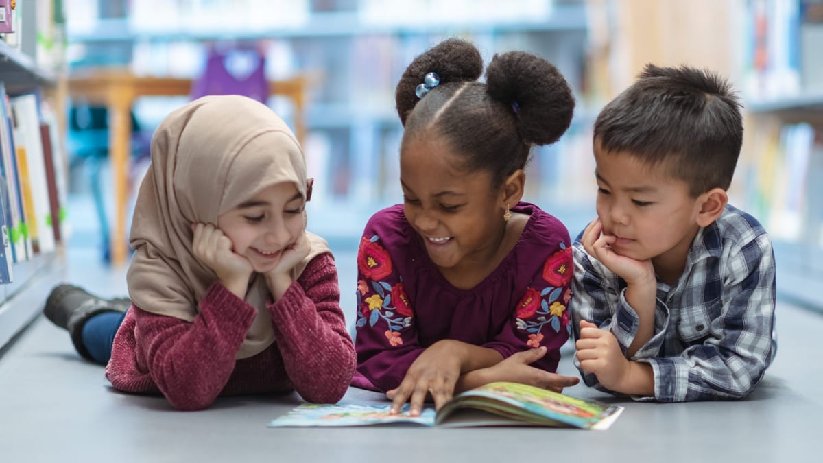 Three ethnically diverse children happily reading together in the school library