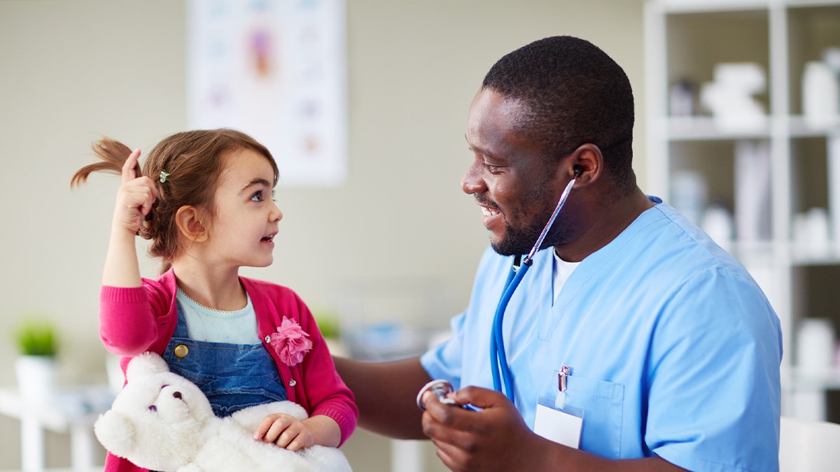 doctor speaking with young girl who is holding a teddy bear