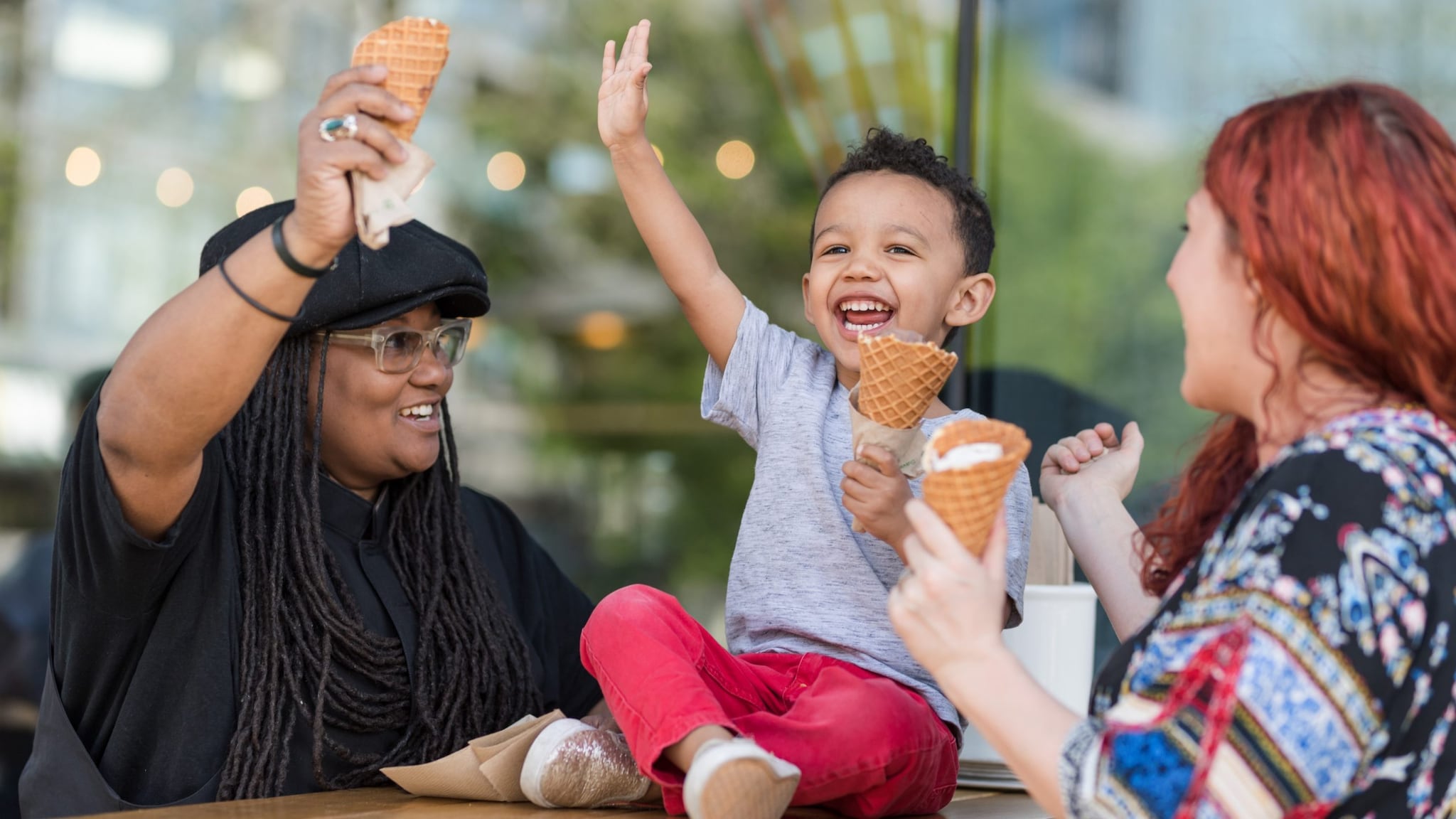Young child happily eating ice cream with two mothers.