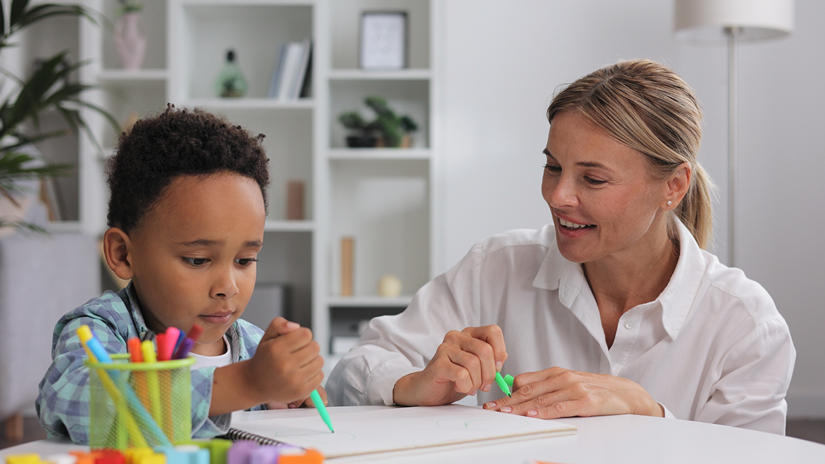 A teacher working with student as he colors