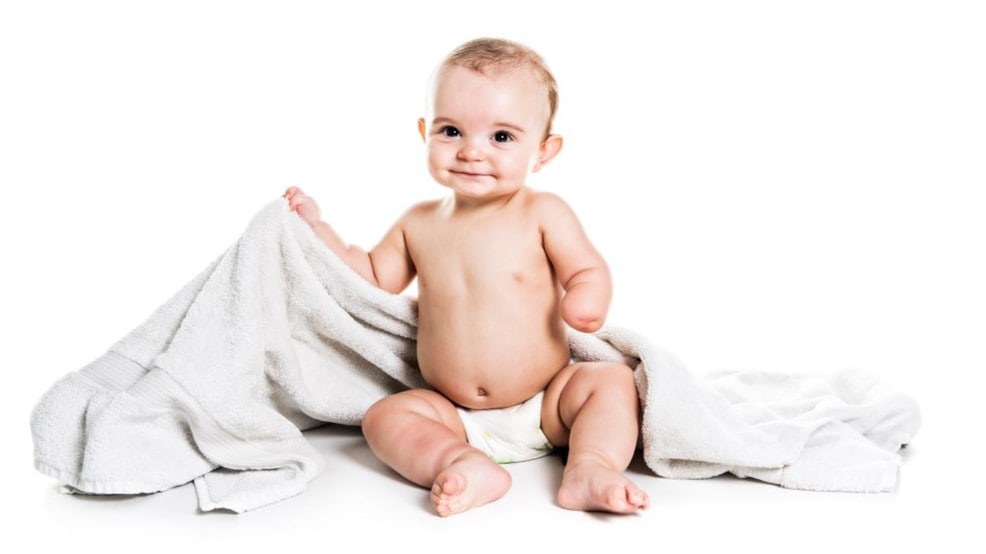 Un bebé contento al que le falta una mano debido a una deficiencia congénita en las extremidades, sentado sobre una manta.