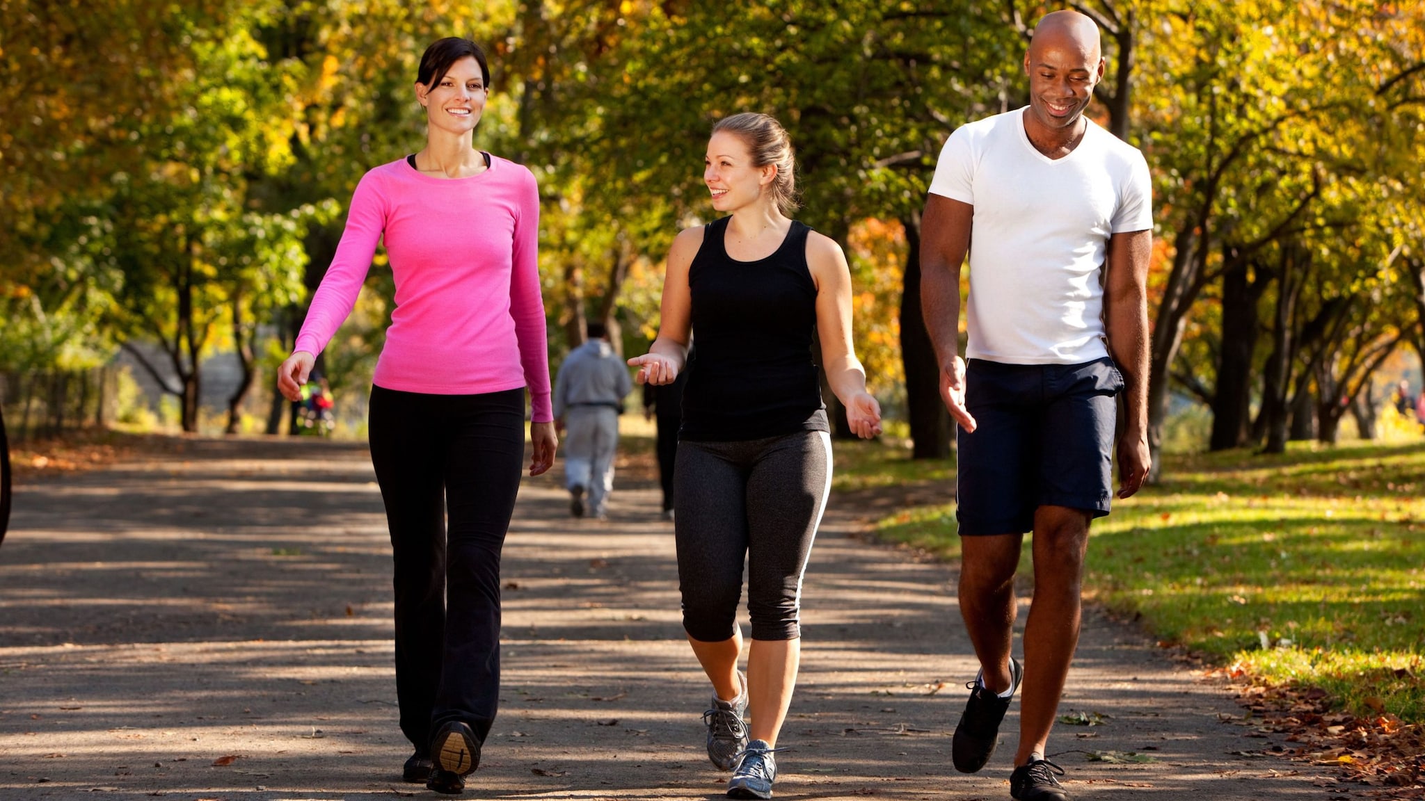 Two physically fit white women walking on a trail with a physically fit black man.