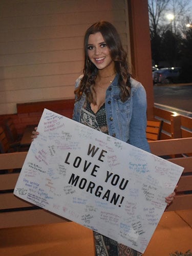Morgan Spencer holding a "We love you Morgan" support sign.