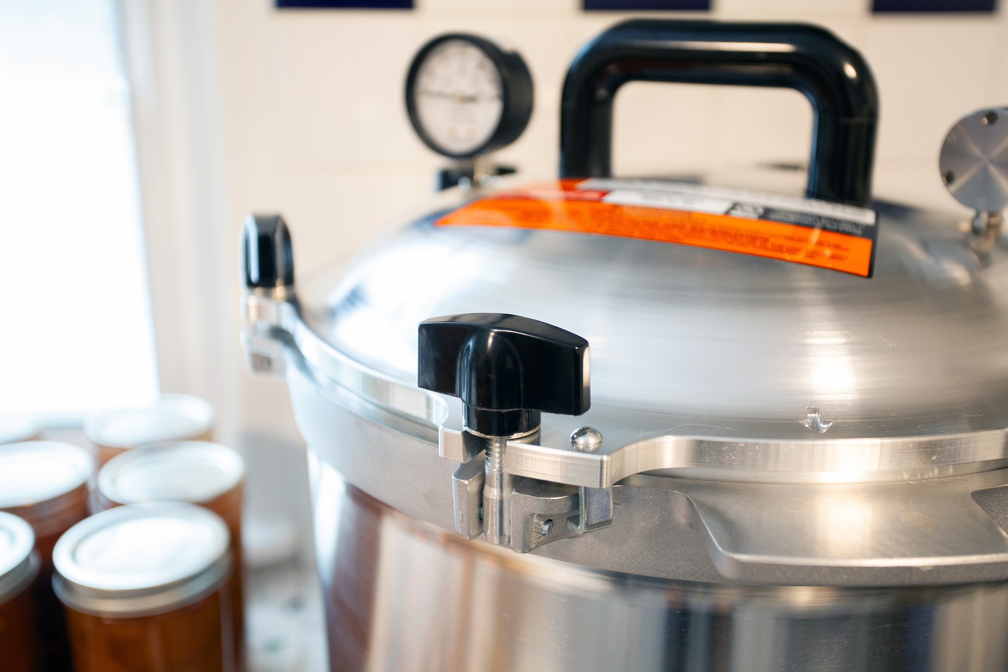 A proper canning pressure cooker next to several jars of homemade canned foods.