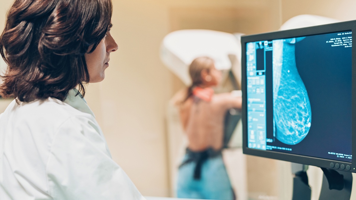 A doctor looks at a computer screen as a woman gets a mammogram