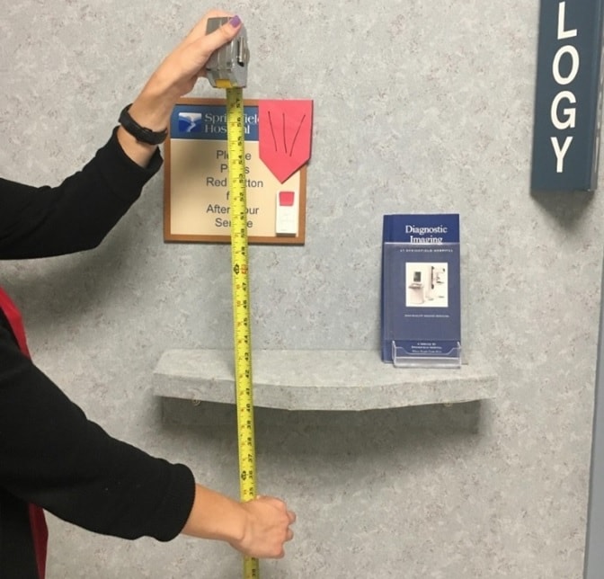 Photo of a person measuring the height of a sign in a mammography clinic to ensure it is accessible to all patients.