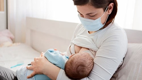 Mother breastfeeding while wearing a mask.