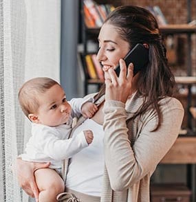 A mother talking on a phone and holding her child