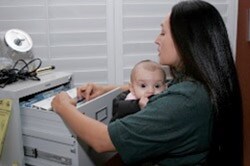 Mother looking through a filing cabinet with an infant