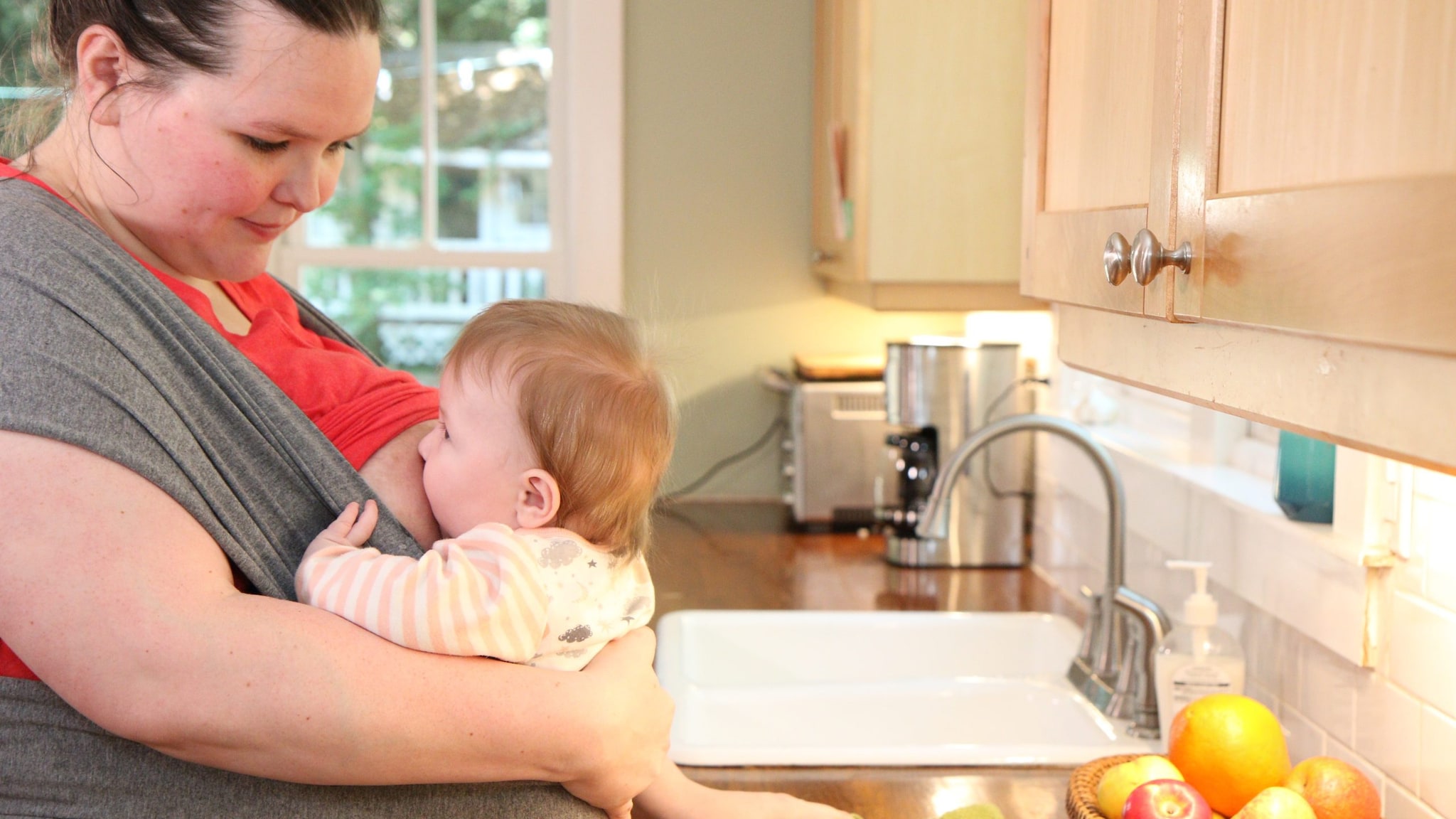 Woman breastfeeds while standing at the kitchen counter.