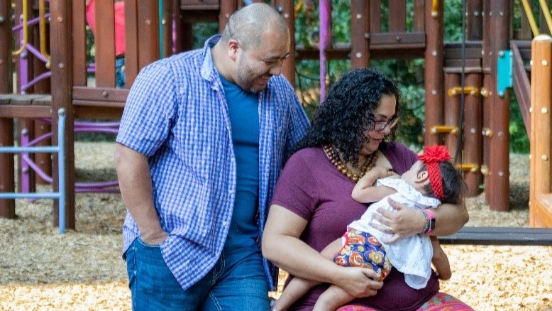 Parents with child at a park while mother is breastfeeding.