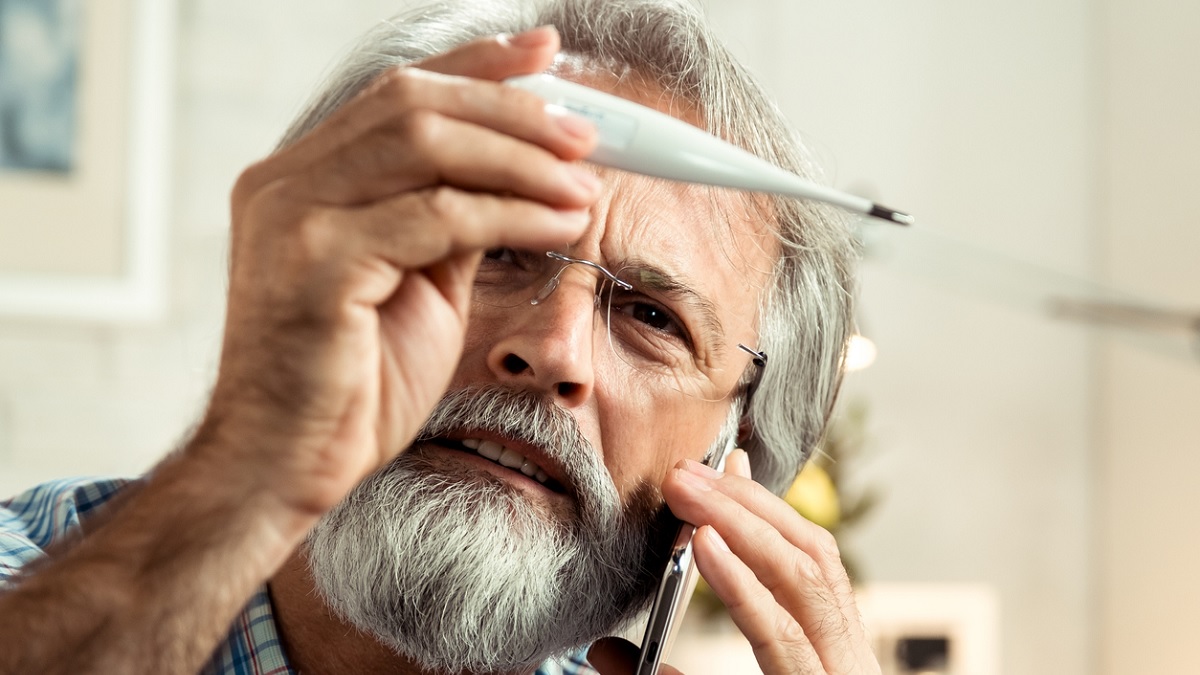 Foto de un hombre mirando un termómetro y llamando a su médico