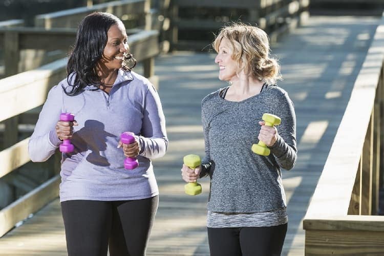 Photo of two women walking with two dumbbells, one on each hand.