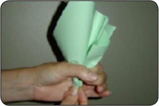 A person folds sheets of green paper to form a paper cabbage