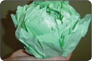 A person folds sheets of green paper to form a paper cabbage